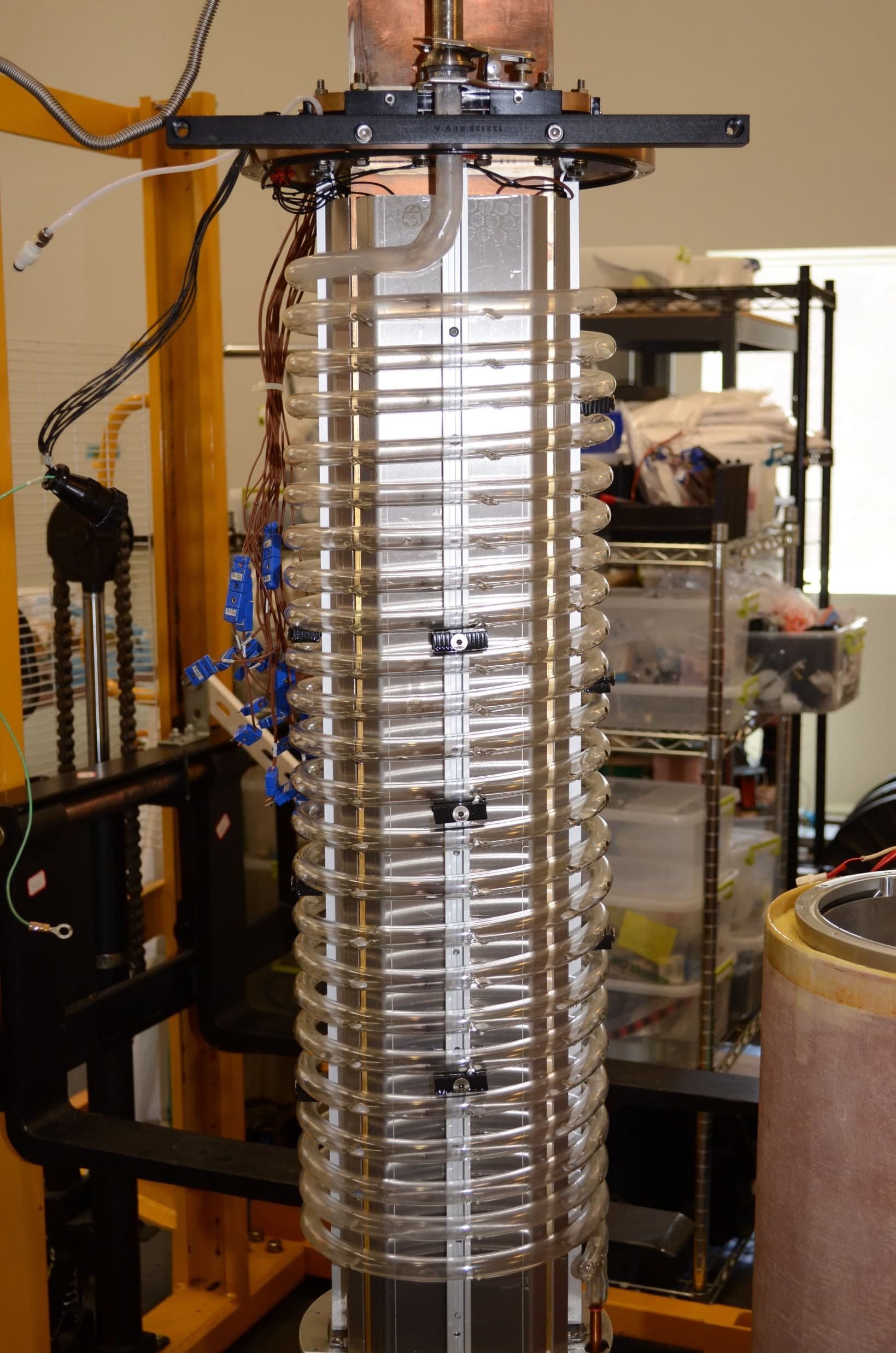 A tall, narrow polarizing column standing upright in a laboratory. A glass tube is wound around it in a long spiral from top to bottom.